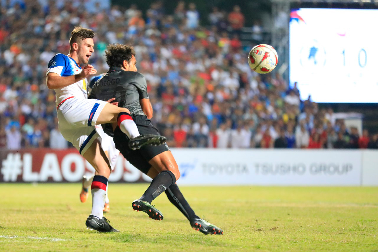 Lanexang United's defender Evans (in white) clears the ball before Buriram United's Diogo Luis Santo reaches it.